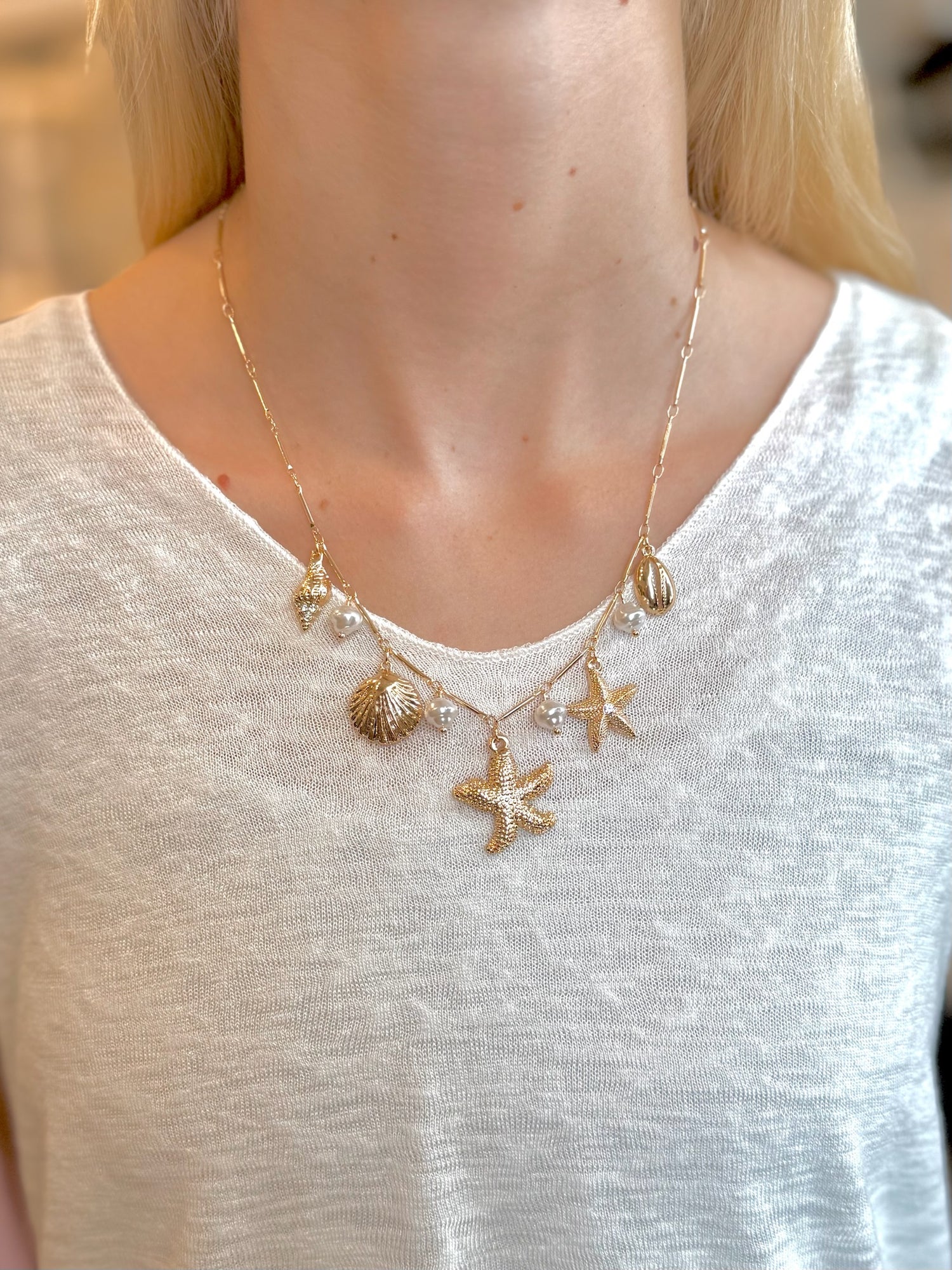 Gold necklace with starfish and shell charms worn by a person on a white background