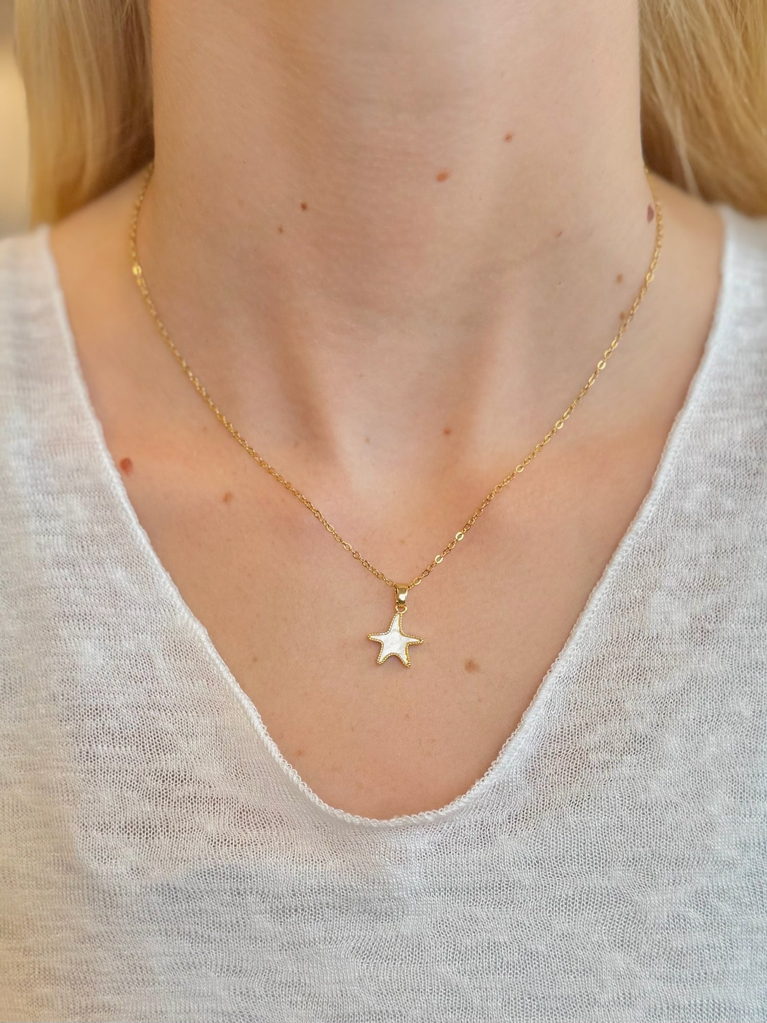 Gold star necklace worn by a person on a plain background