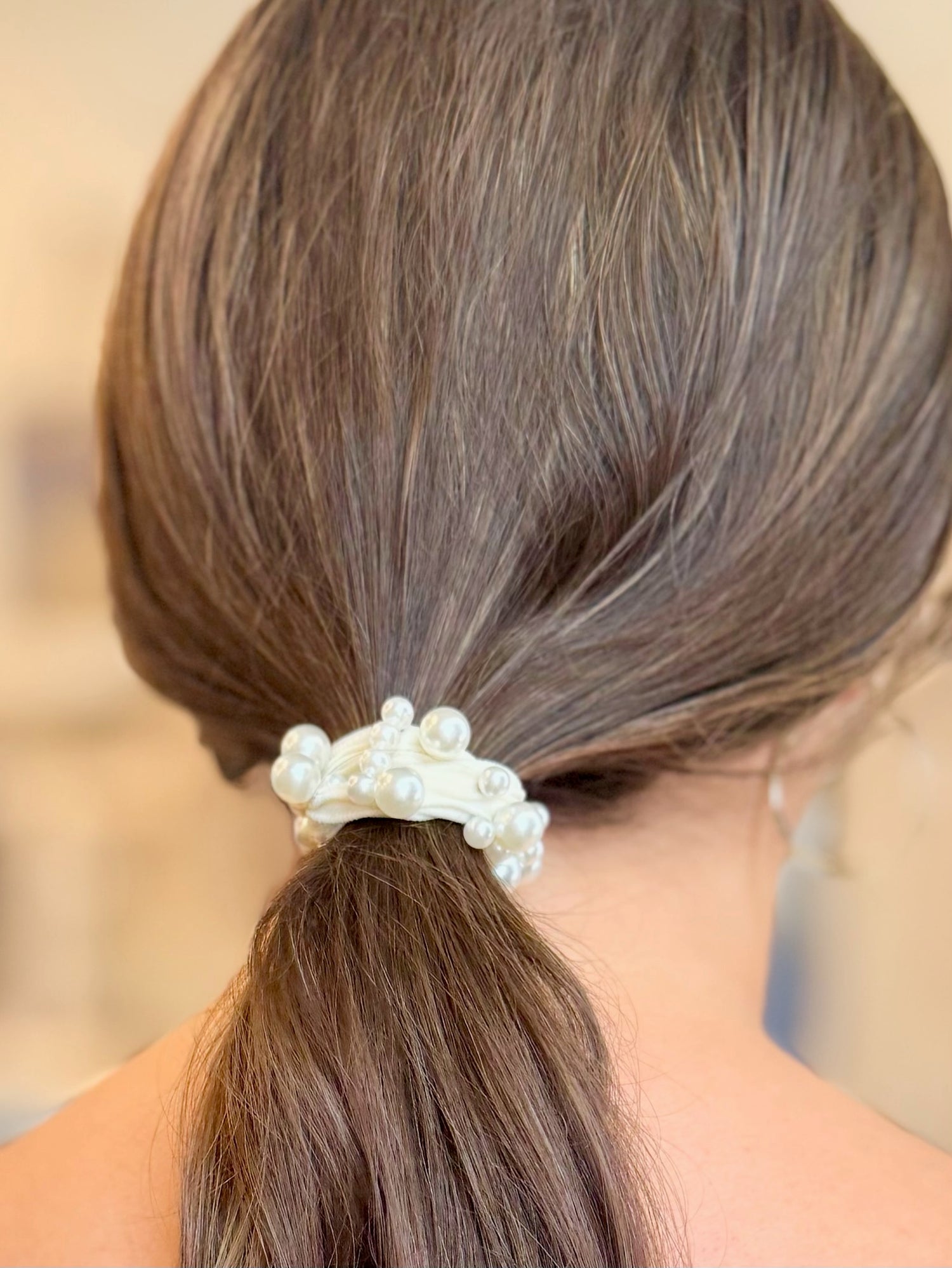 Close-up of a ponytail with a decorative hair tie featuring pearls.