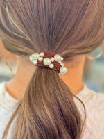 Close-up of a hair tie with pearls in a brown ponytail against a blurred background