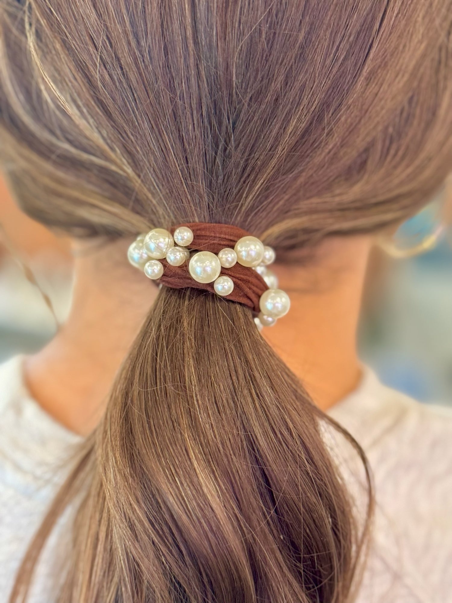 Close-up of a hair tie with pearls in a brown ponytail against a blurred background