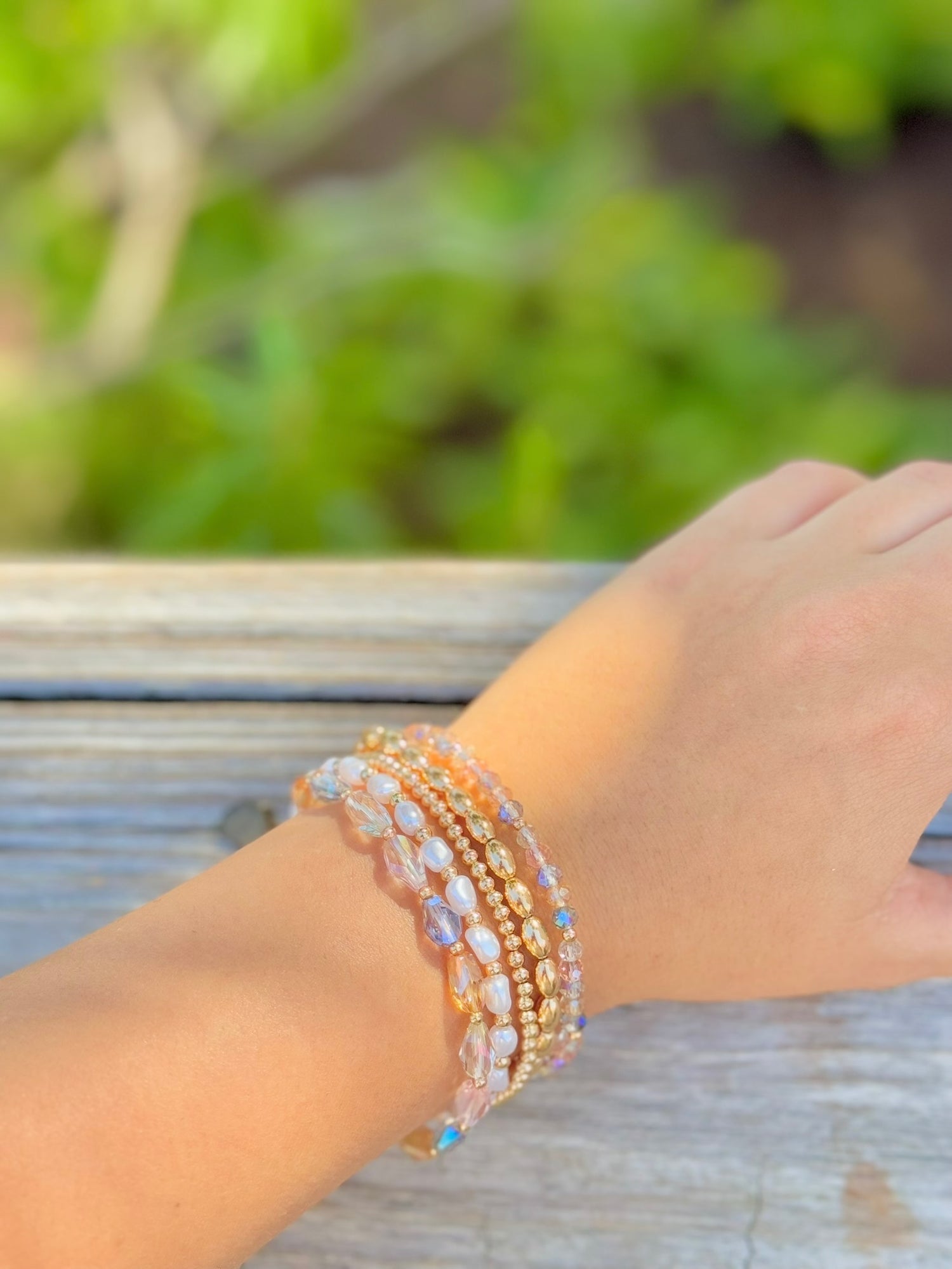 Close-up of a wrist wearing multiple beaded bracelets with a blurred green background