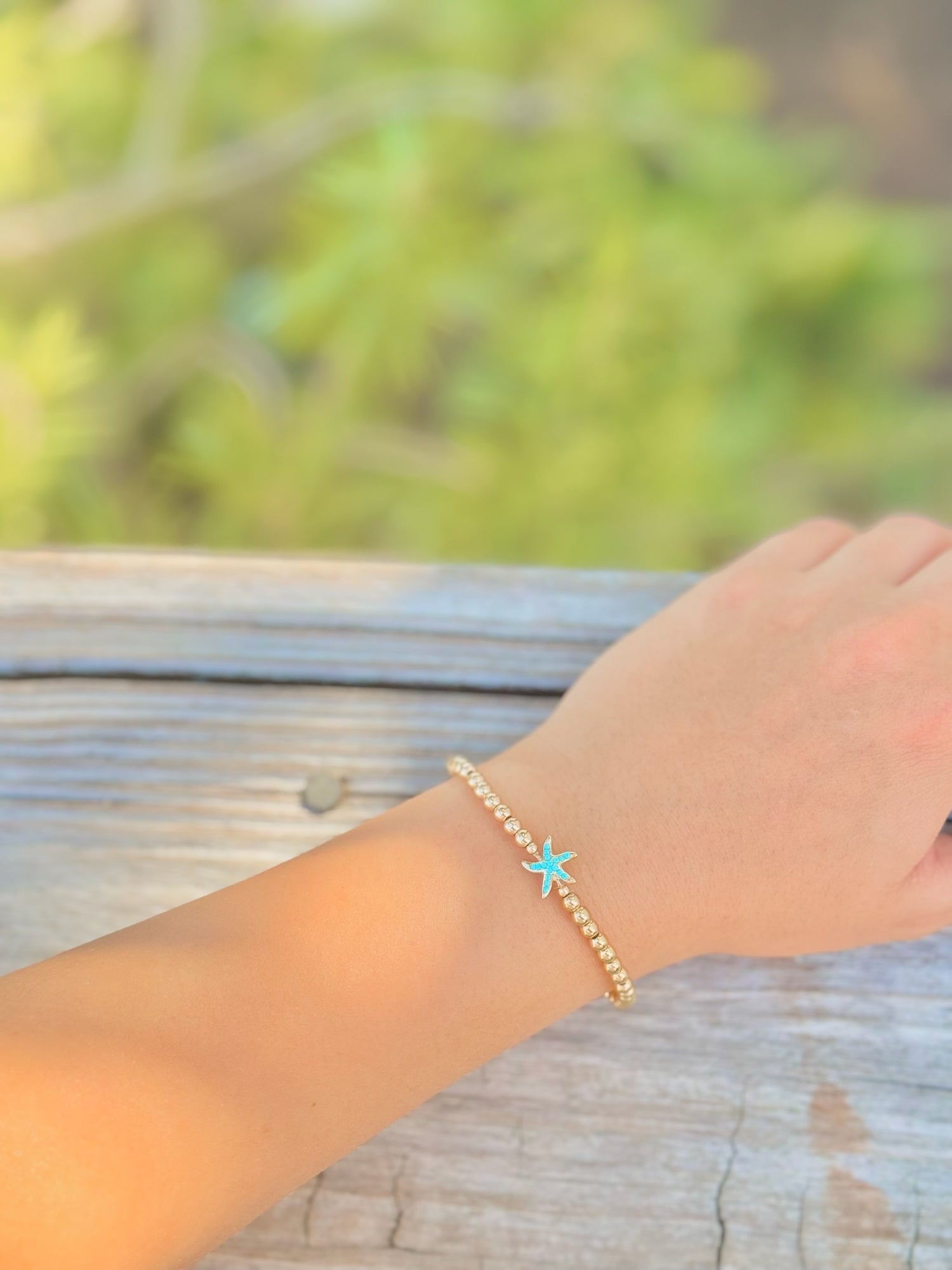 Gold bracelet with a turquoise charm on a wrist against a blurred natural background