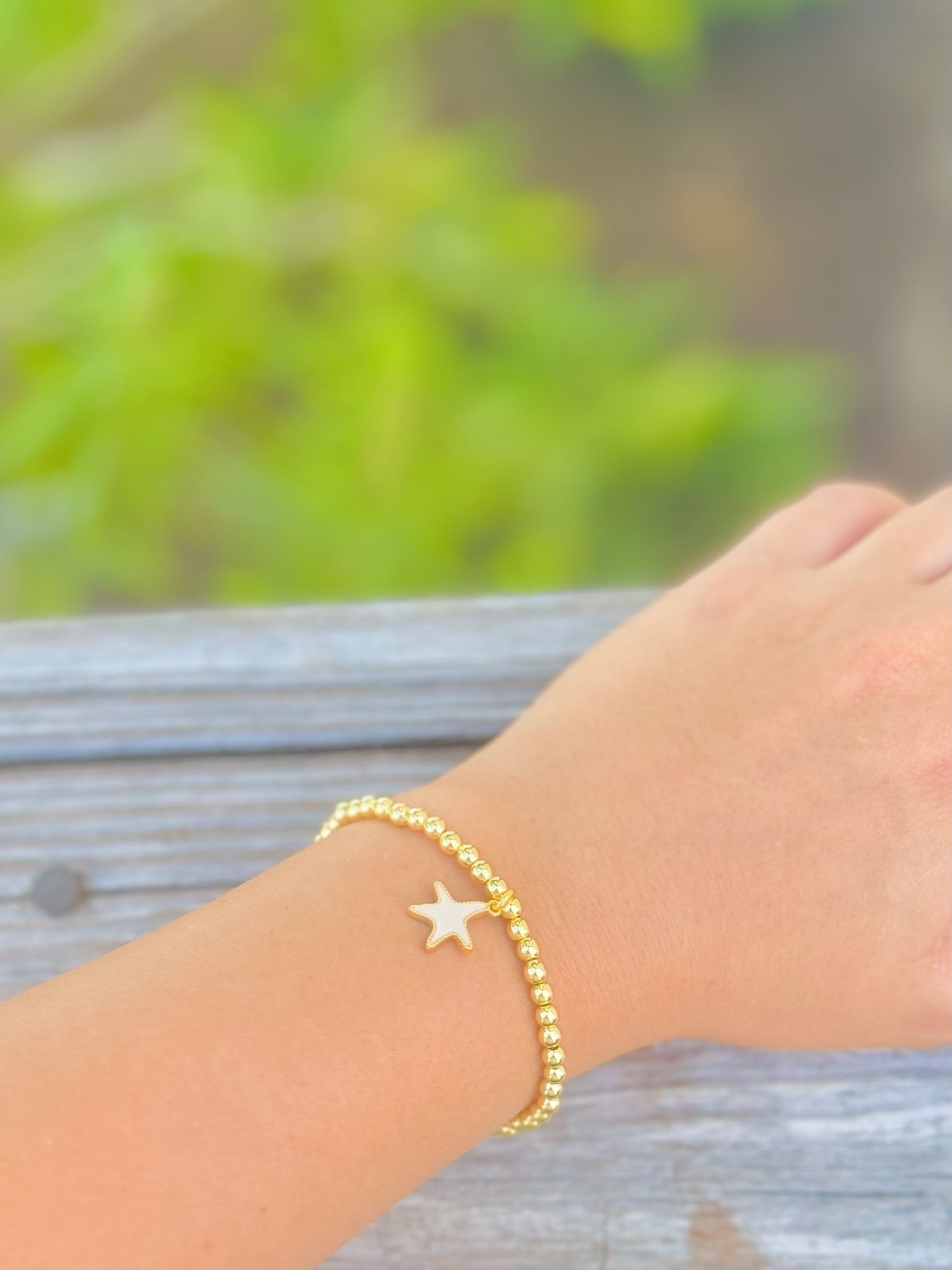 Gold bracelet with a star charm on a wrist against a blurred natural background