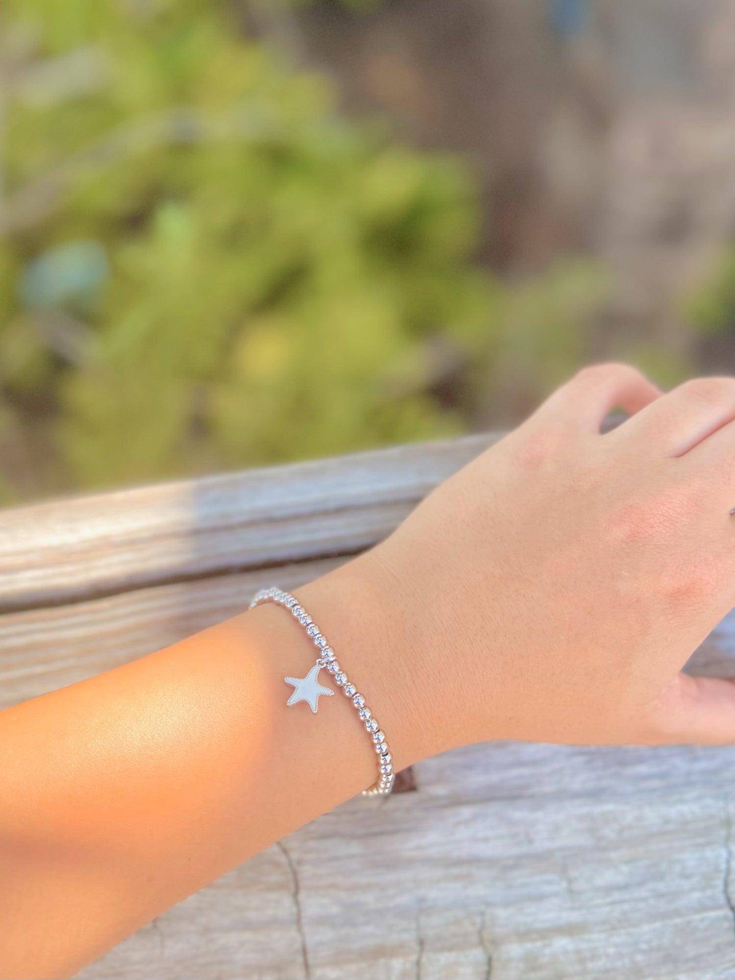 Hand wearing a silver bracelet with a star charm against a blurred natural background