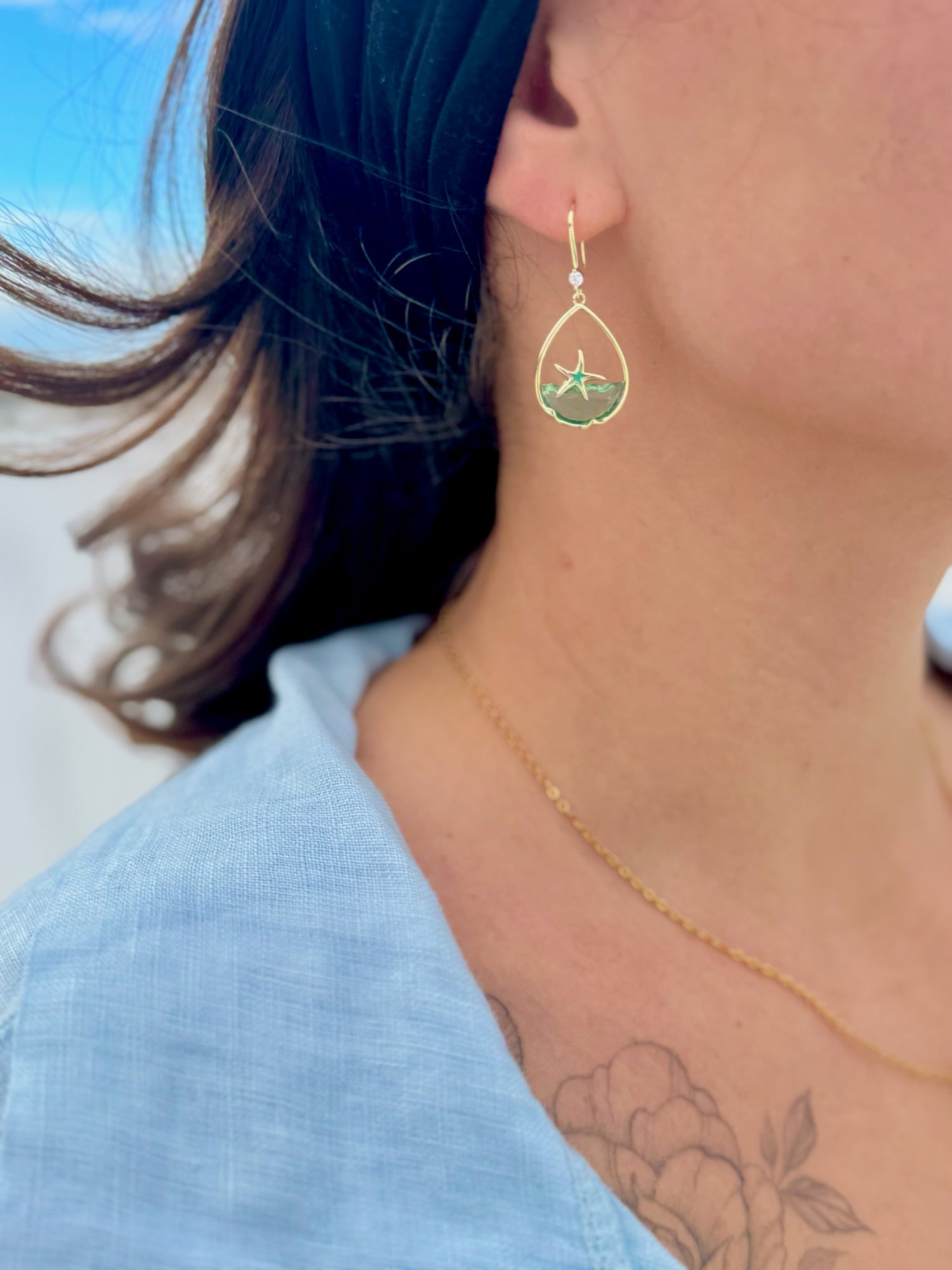 Close-up of a person wearing gold earrings and a necklace with a blue shirt.