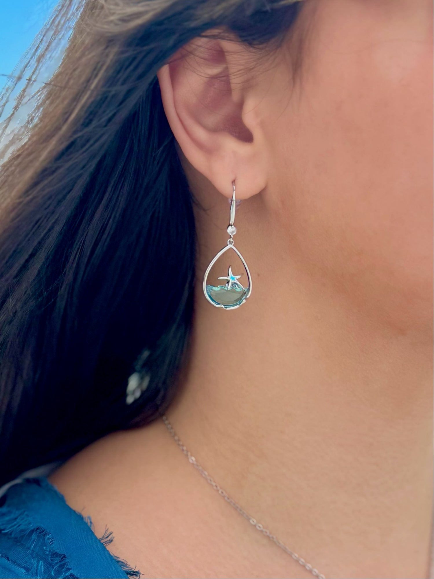 Close-up of a person wearing a silver earring with a teardrop design.