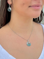 Close-up of a person wearing a silver necklace with a pendant, with earrings visible.