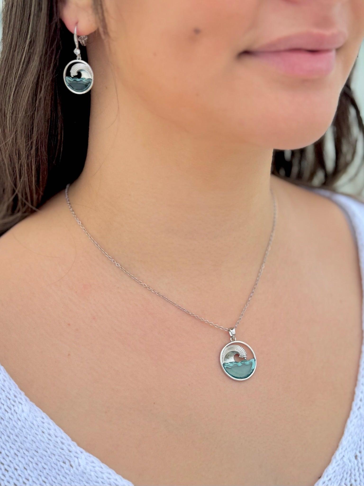 Close-up of a person wearing a silver necklace with a pendant, with earrings visible.