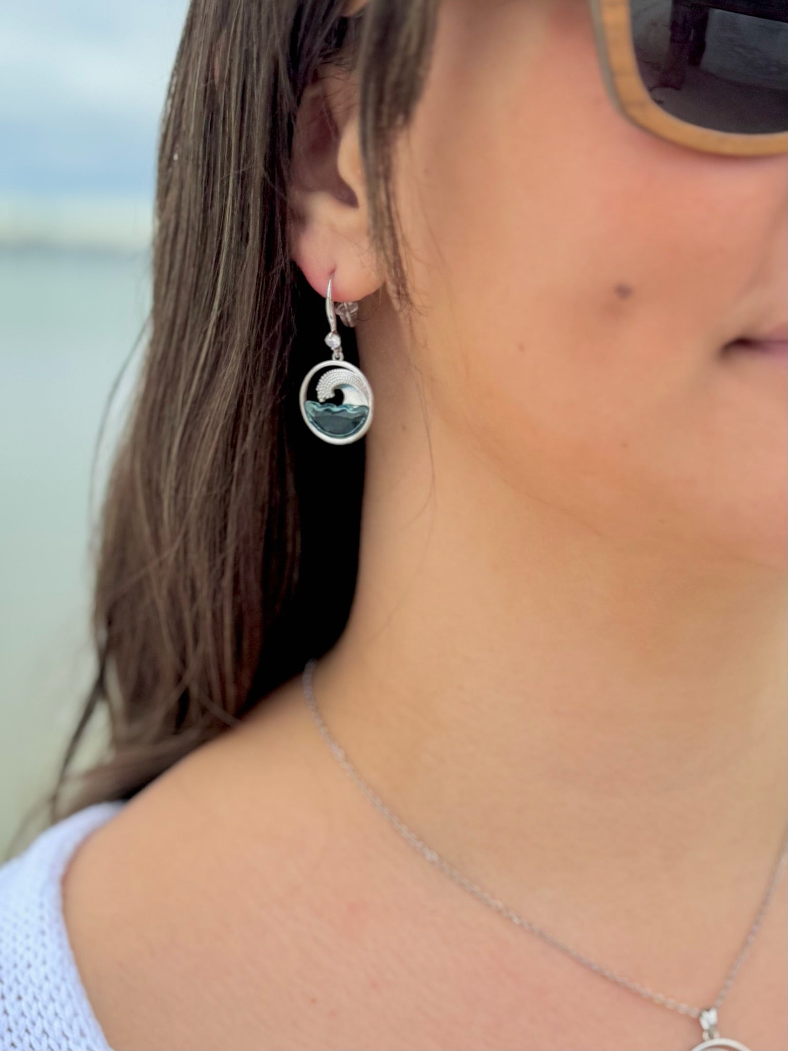 Close-up of a person wearing silver earrings with a scenic design, outdoors.