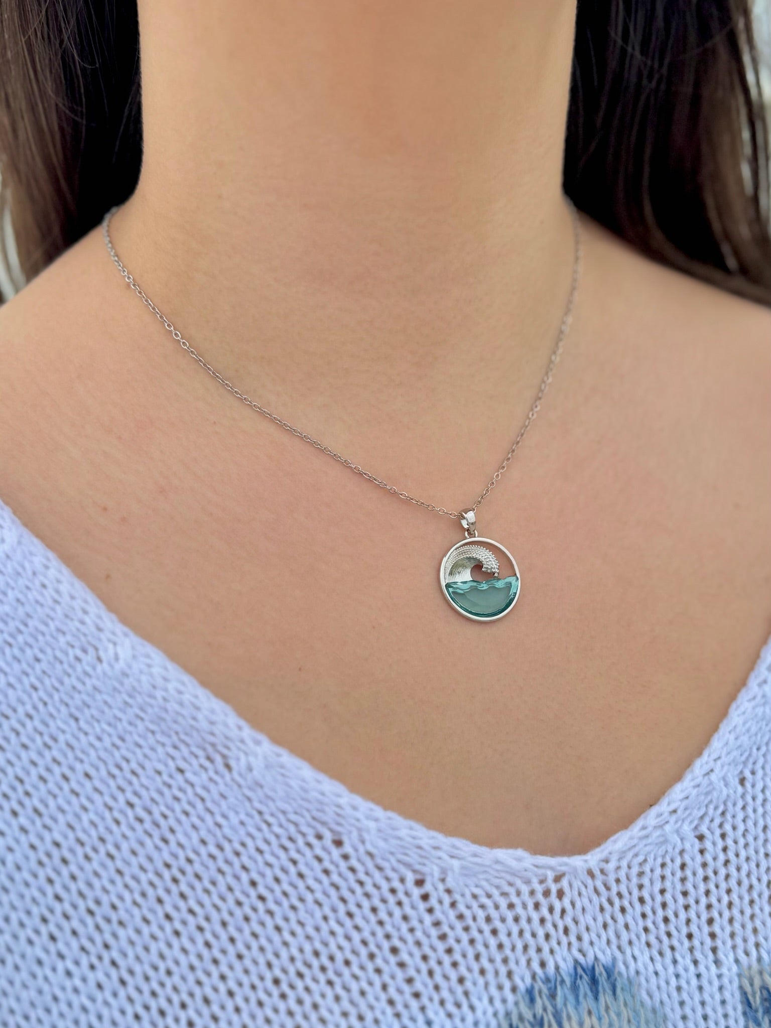 Necklace with a pendant featuring a scenic design worn by a person in a light blue top.