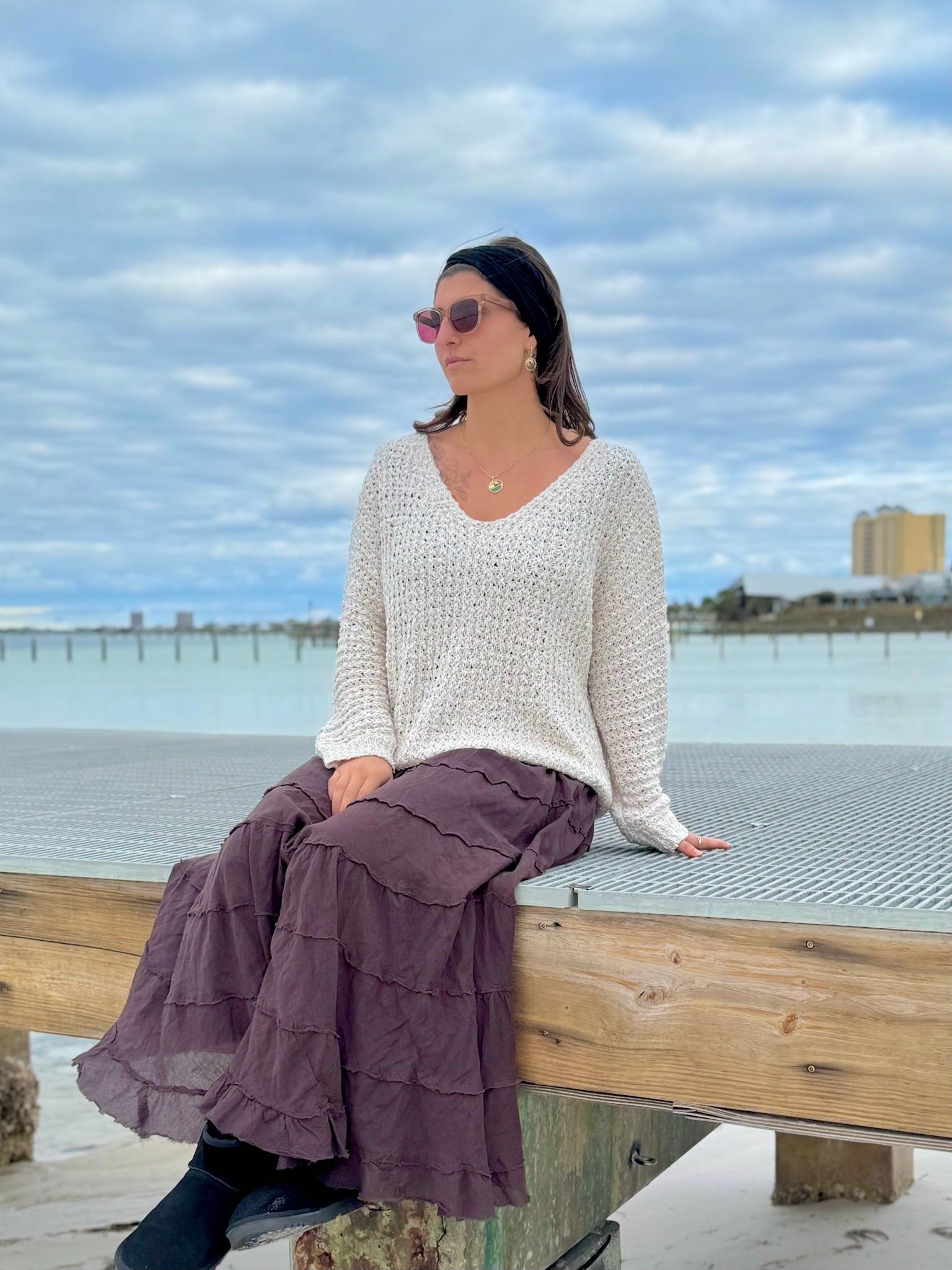 Woman sitting on dock by beach with ivory sweater and brown long skirt
