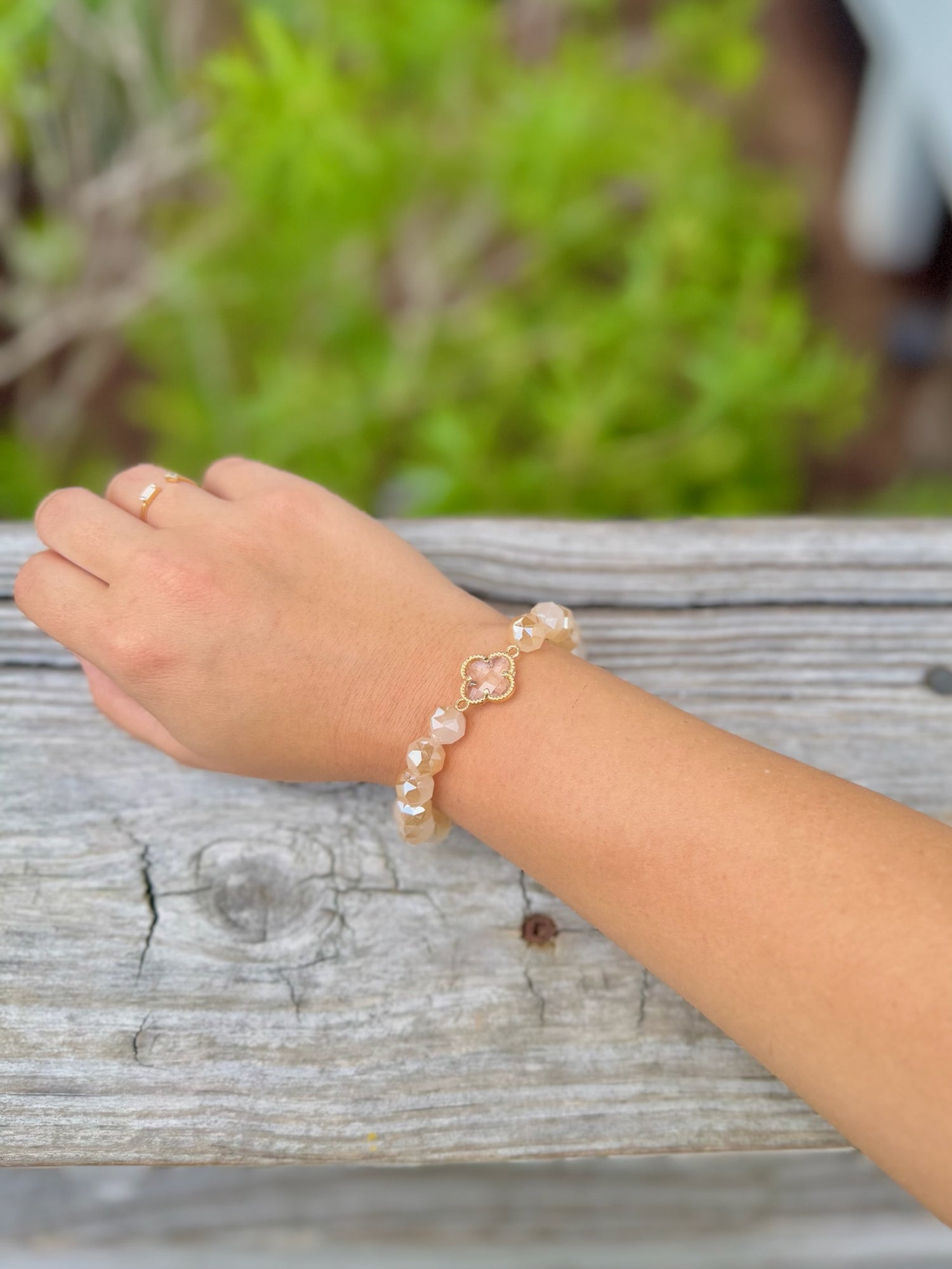 Amara Clover Bracelet with neutral faceted beads and gold-tone clover charm on model wrist 