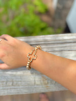 Gold beaded stretch bracelet with polished cross charm on woman's arm 