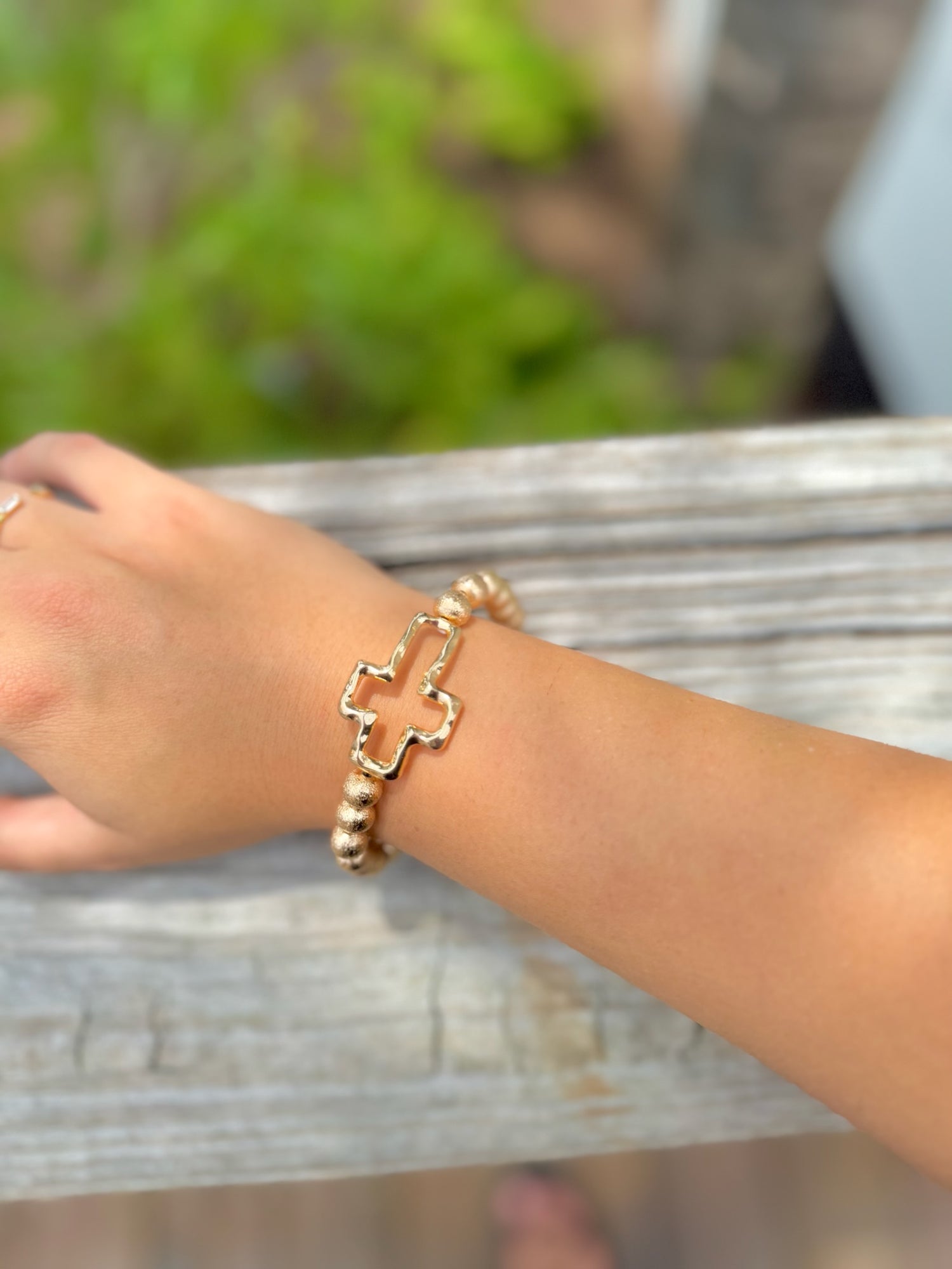 Gold beaded stretch bracelet with polished cross charm on woman's arm 