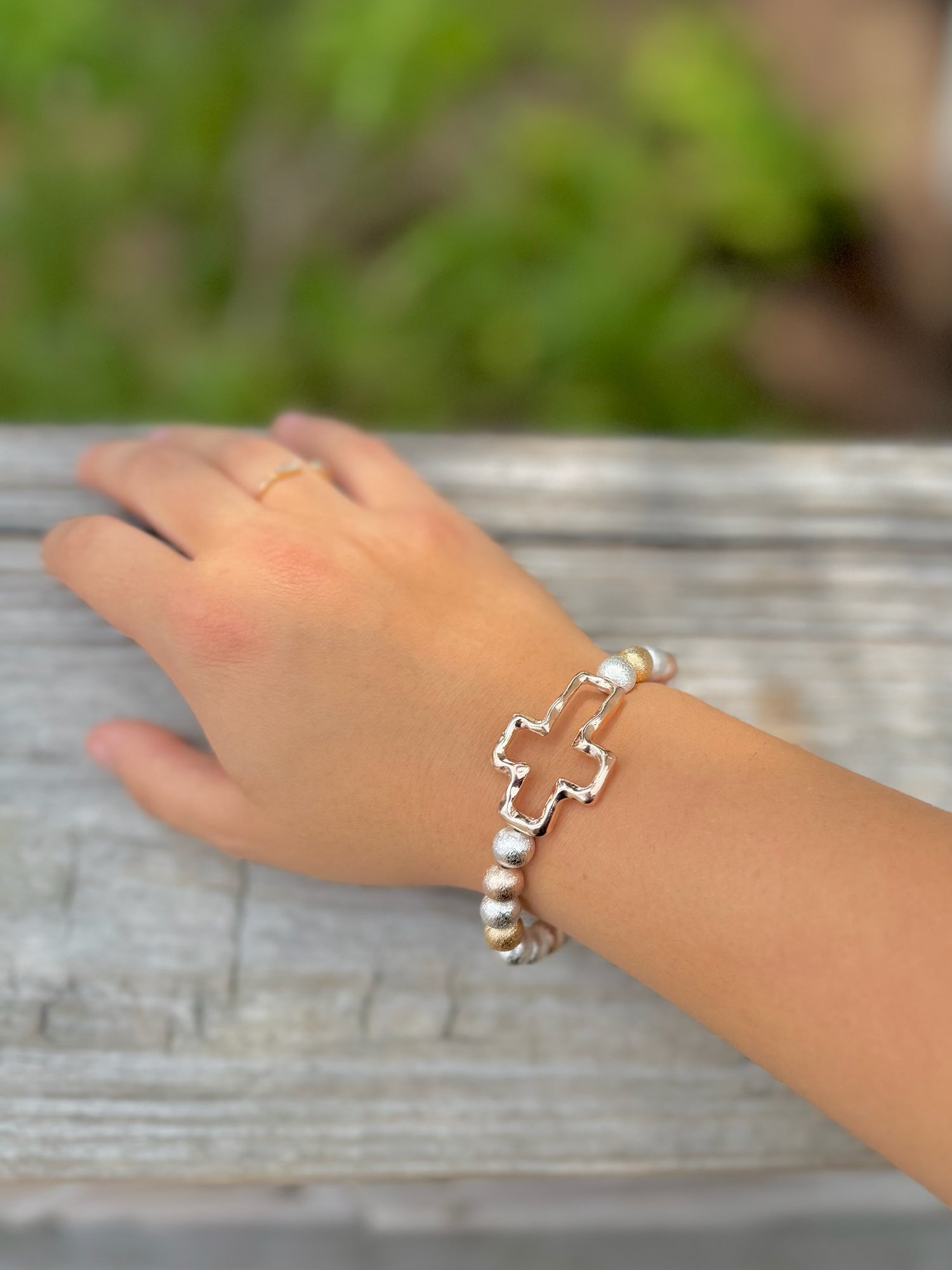 Silver and gold beaded stretch bracelet with polished cross charm on woman's arm 