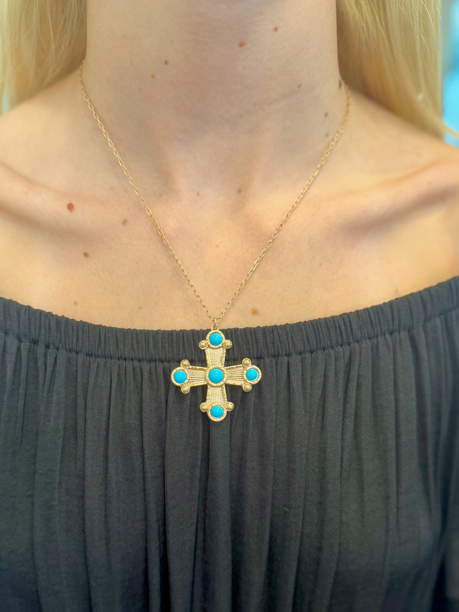 Zara Cross Necklace with turquoise stone accents on gold-tone chain on a woman's neck 