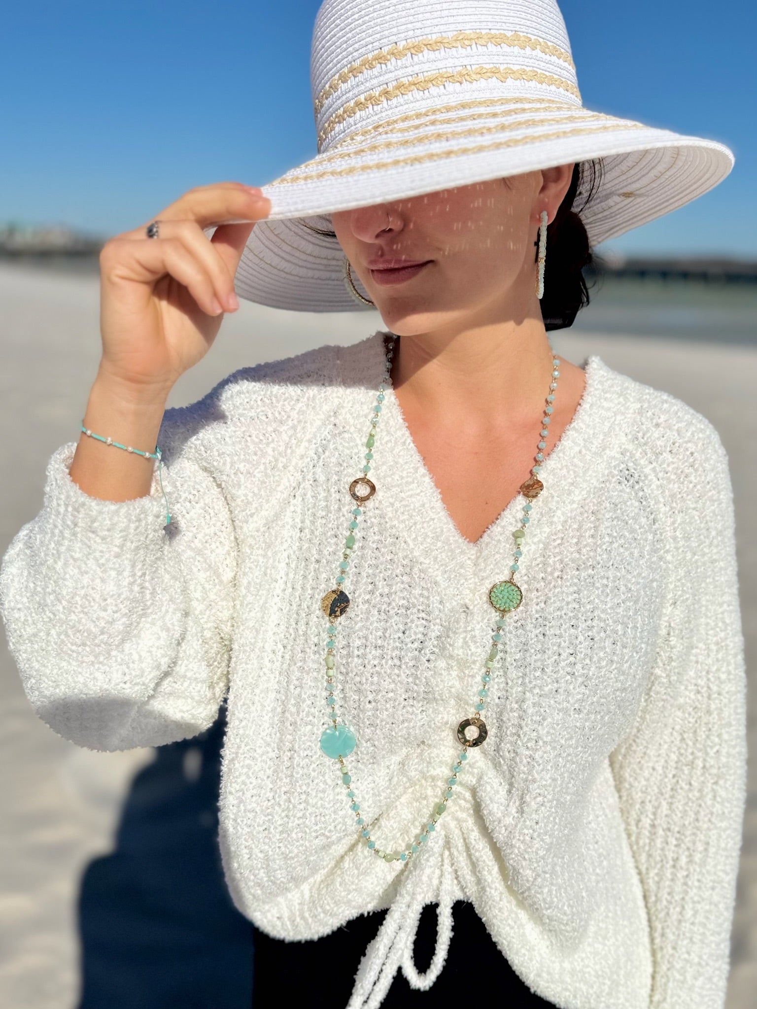 Woman wearing a white knit cardigan and sun hat on a beach