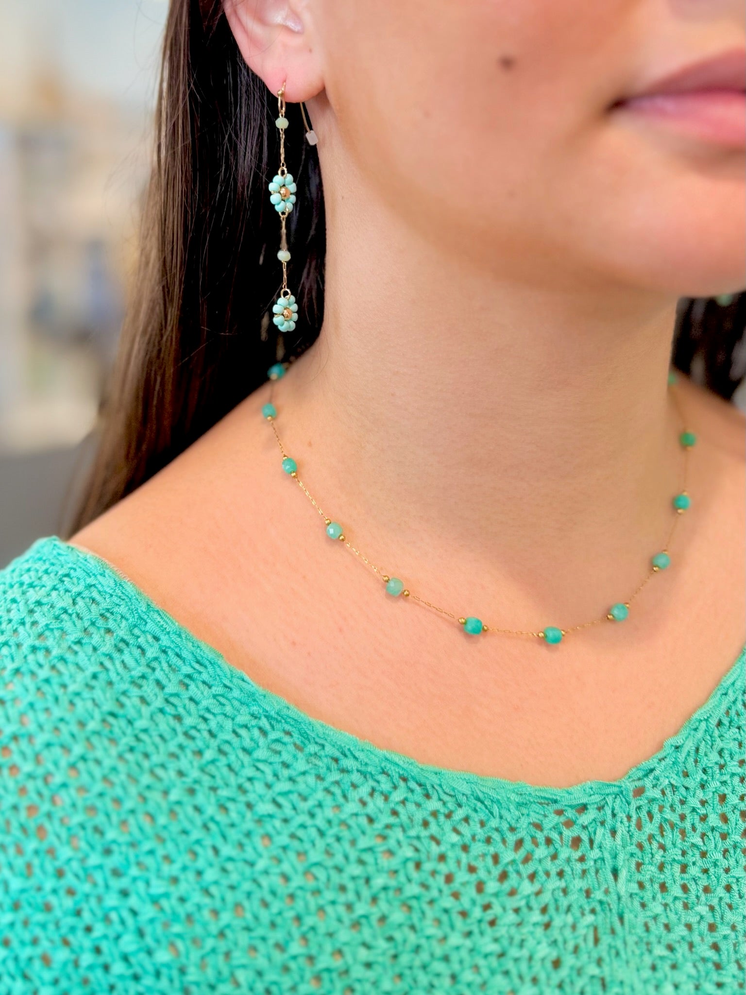 Close-up of a person wearing turquoise beaded earrings and necklace with a blurred background