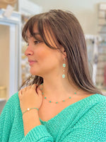Woman wearing a green knitted sweater and turquoise jewelry in an indoor setting
