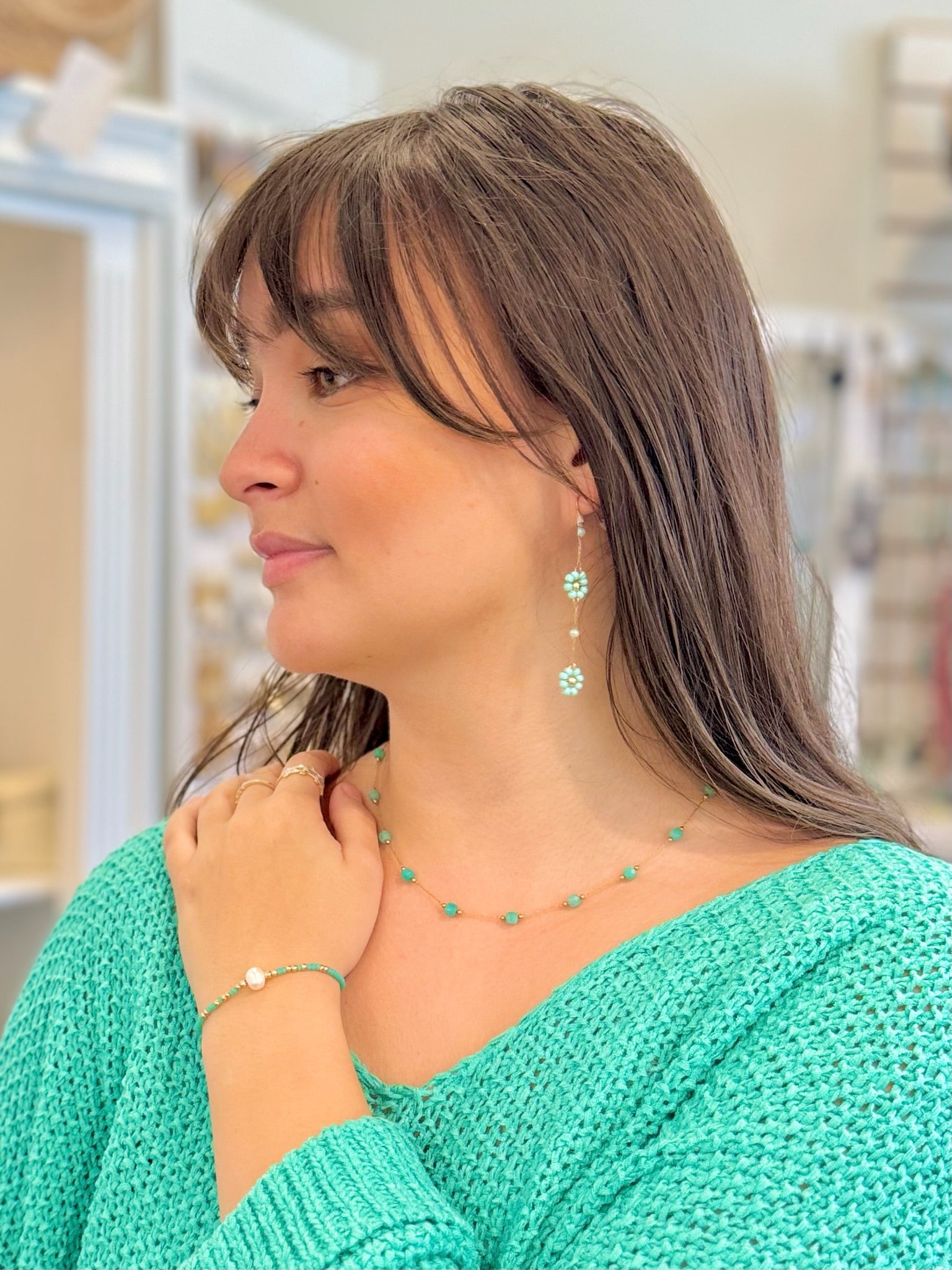 Woman wearing a green knitted sweater and turquoise jewelry in an indoor setting