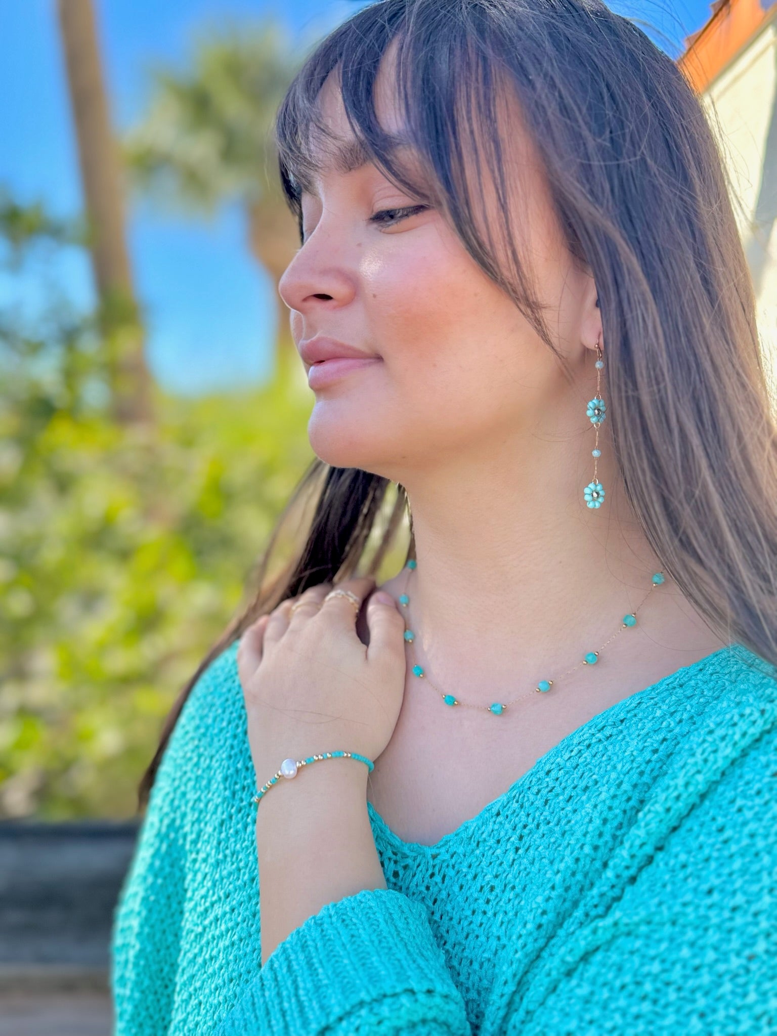 Woman wearing turquoise jewelry set outdoors with greenery in the background
