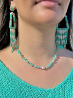 Close-up of a person wearing turquoise beaded earrings and necklace.