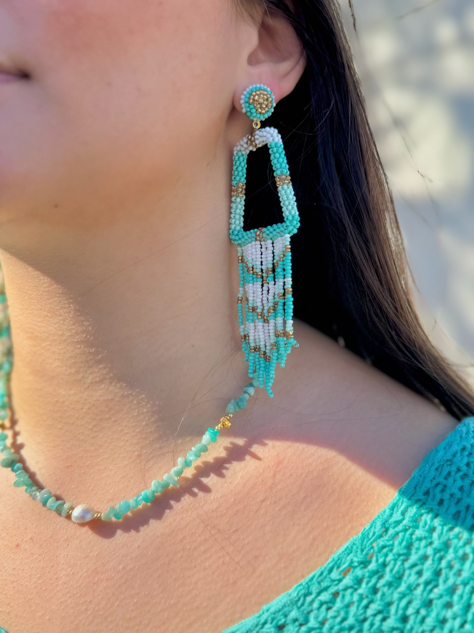 Close-up of a person wearing turquoise beaded earrings and necklace.