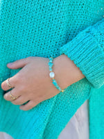 Close-up of a hand wearing a turquoise bracelet with a matching teal sweater.