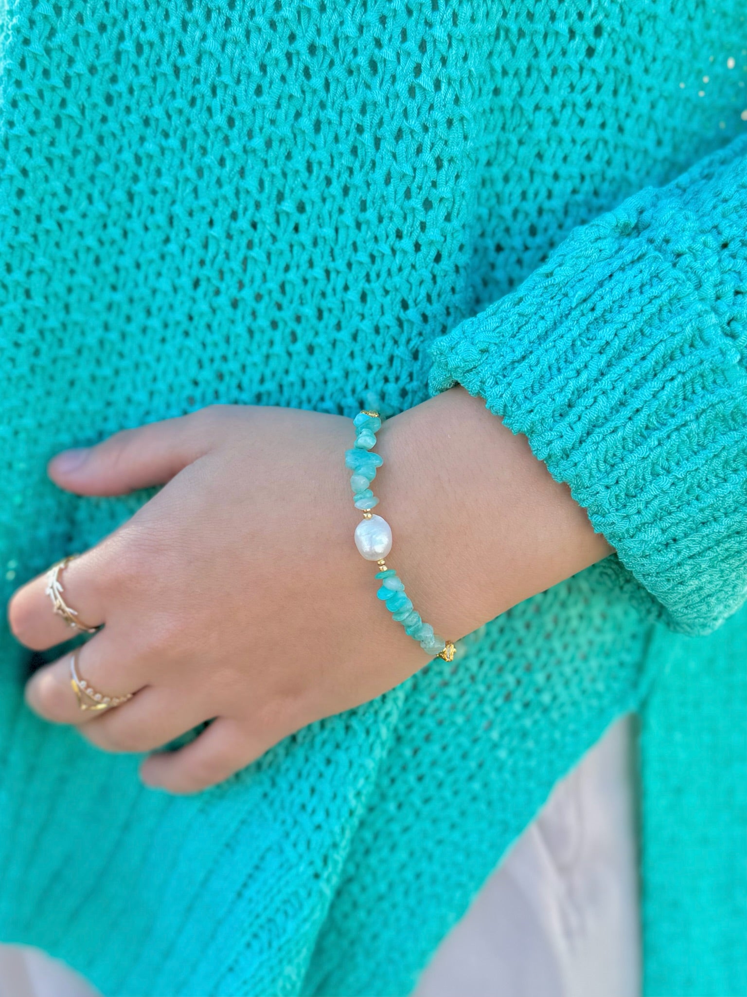 Close-up of a hand wearing a turquoise bracelet with a matching teal sweater.