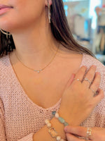 Close-up of a person wearing jewelry including earrings, a necklace, rings, and a bracelet.
