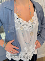Person wearing a denim jacket over a white lace top with a necklace.