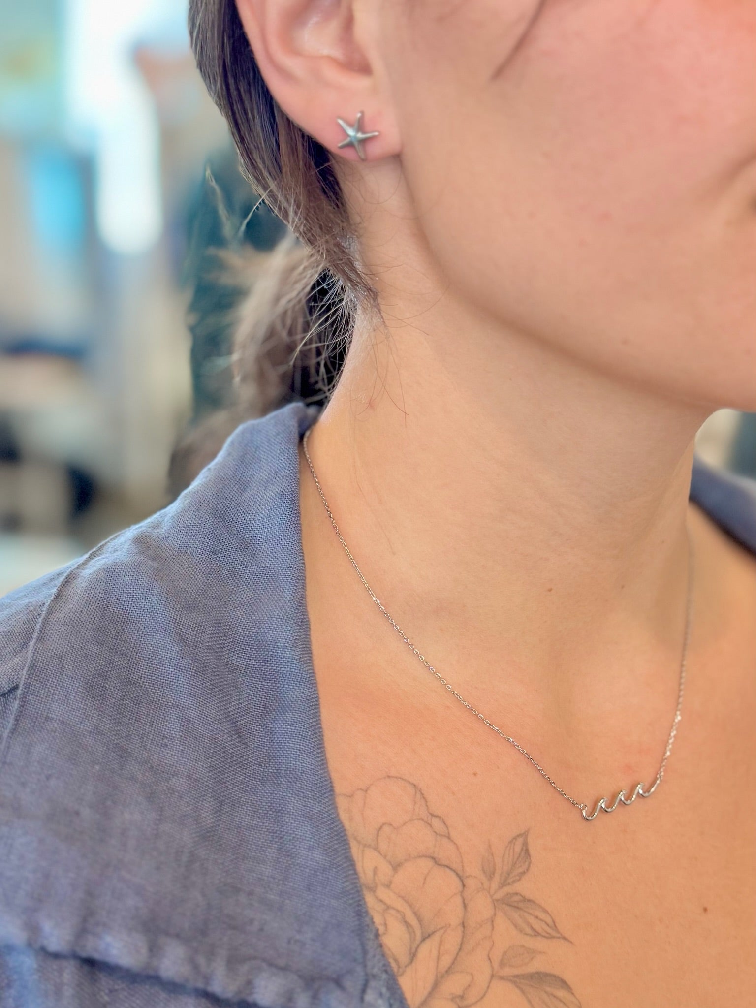 Close-up of a person wearing a star-shaped earring and a delicate necklace with a blurred background.