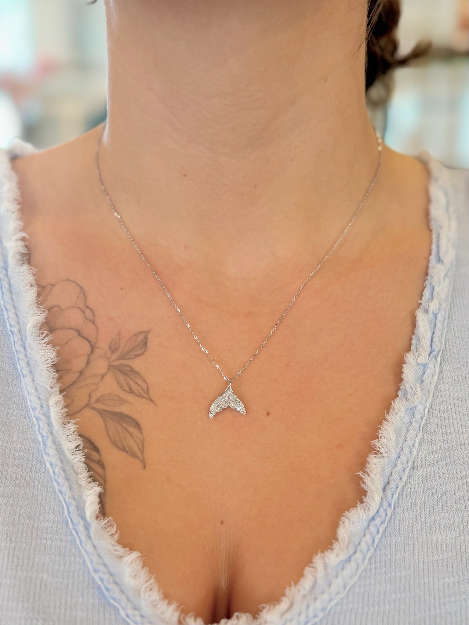 sparkly sterling silver dolphin tail pendant necklace worn with a V-neck top, showing length and fit.