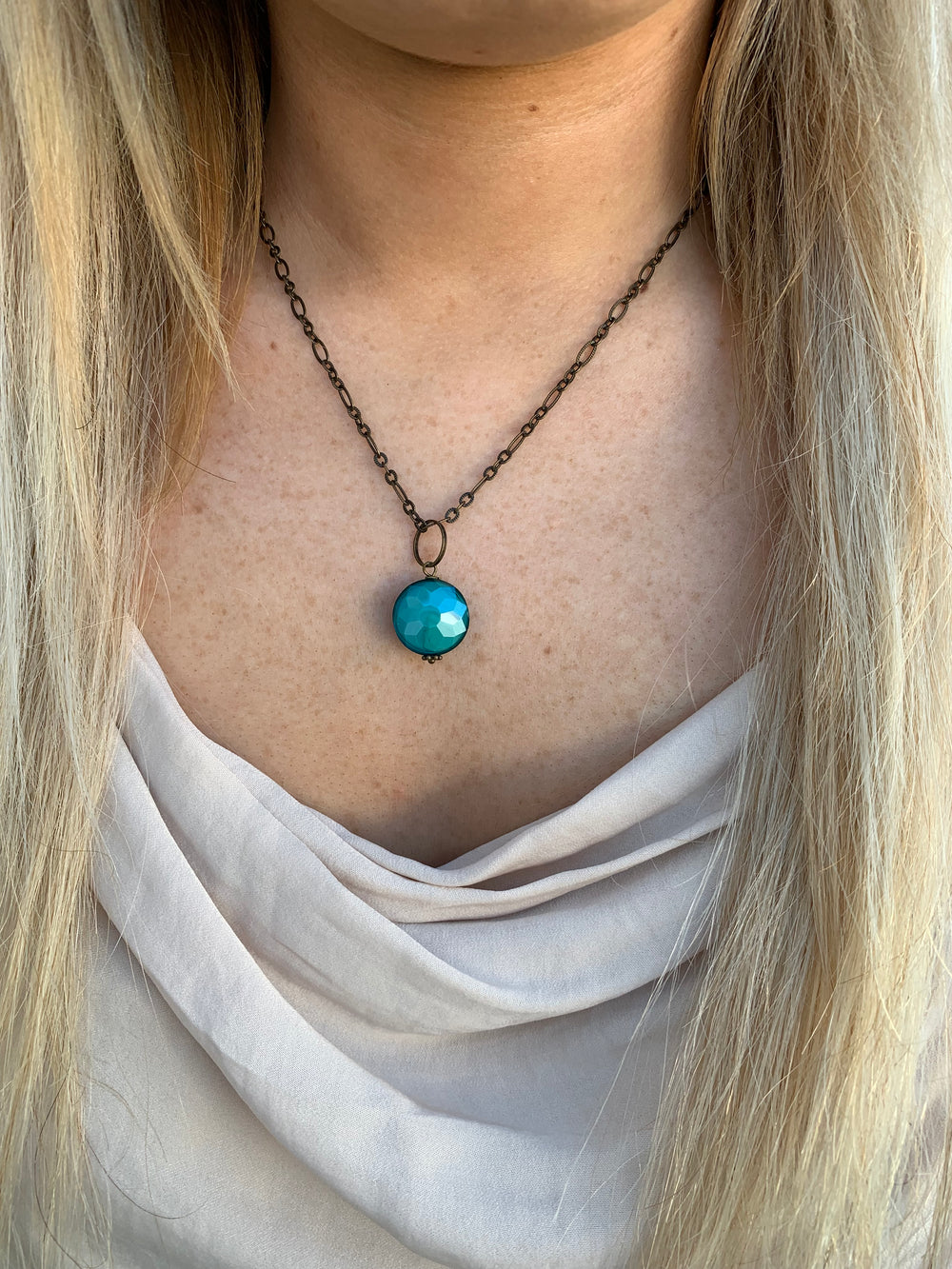 Color drop brass necklace in teal on model. 