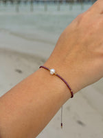 Close-up of a wrist wearing a bracelet with a pearl on a blurred beach background