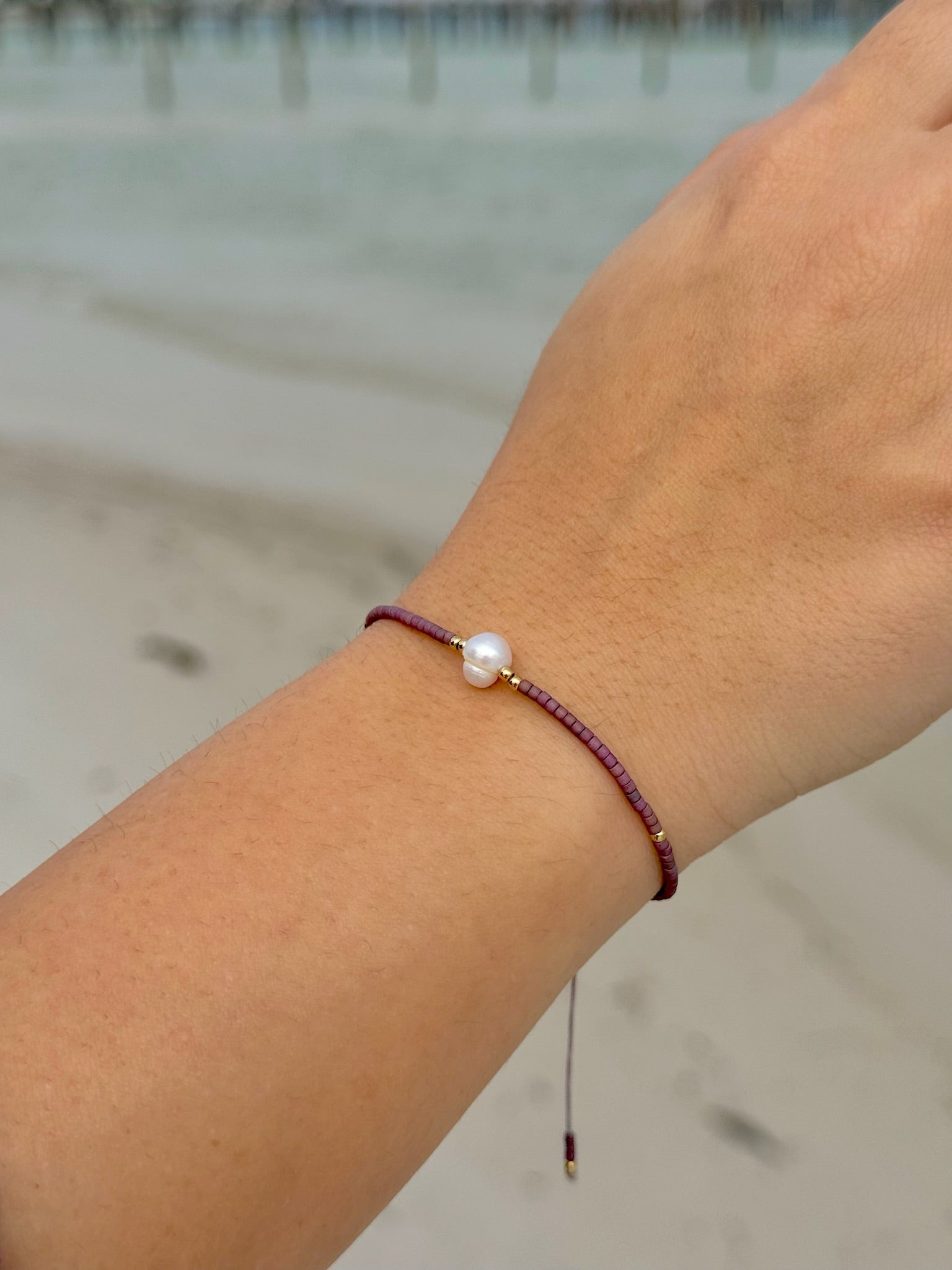 Close-up of a wrist wearing a bracelet with a pearl on a blurred beach background