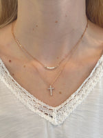 Close-up of a person wearing a gold necklace with a cross pendant on a white lace garment.