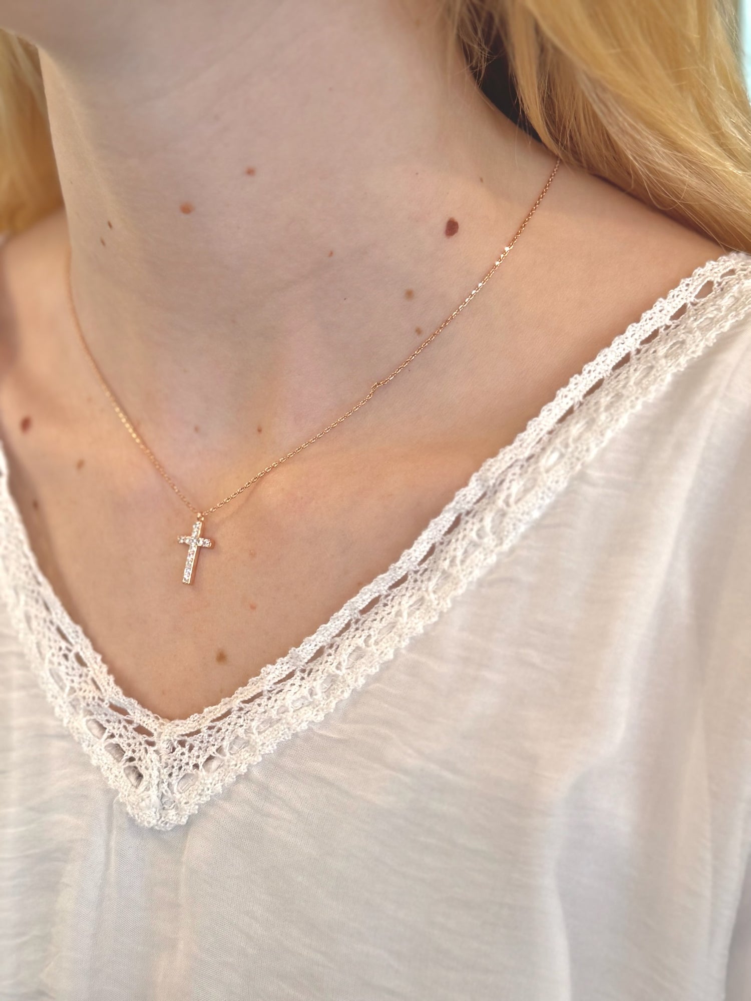 Close-up of a person wearing a delicate gold necklace with a small cross pendant.