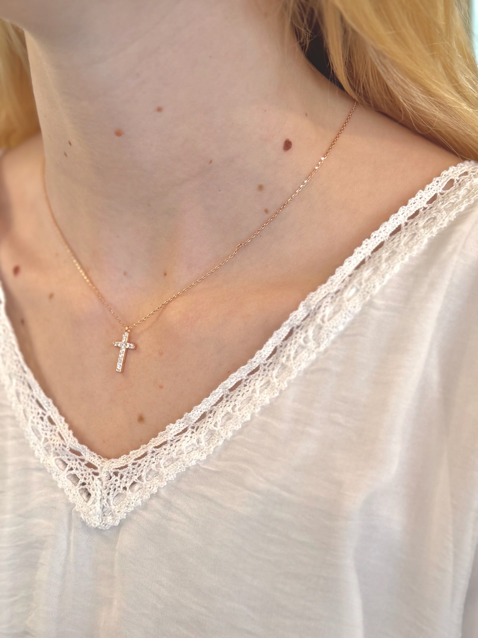 Close-up of a person wearing a delicate gold necklace with a small cross pendant.