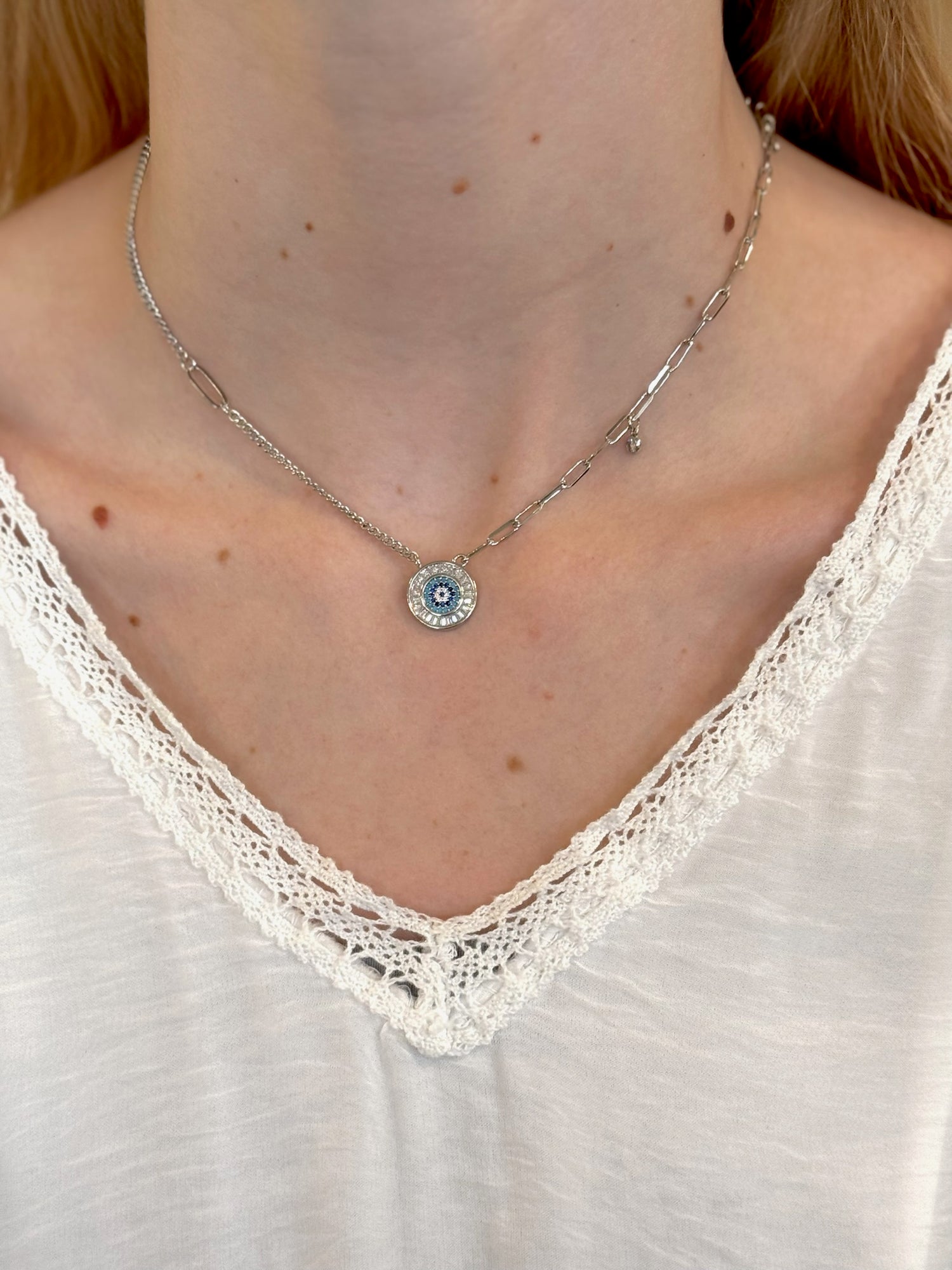 Necklace with a small pendant worn by a person in a white lace top