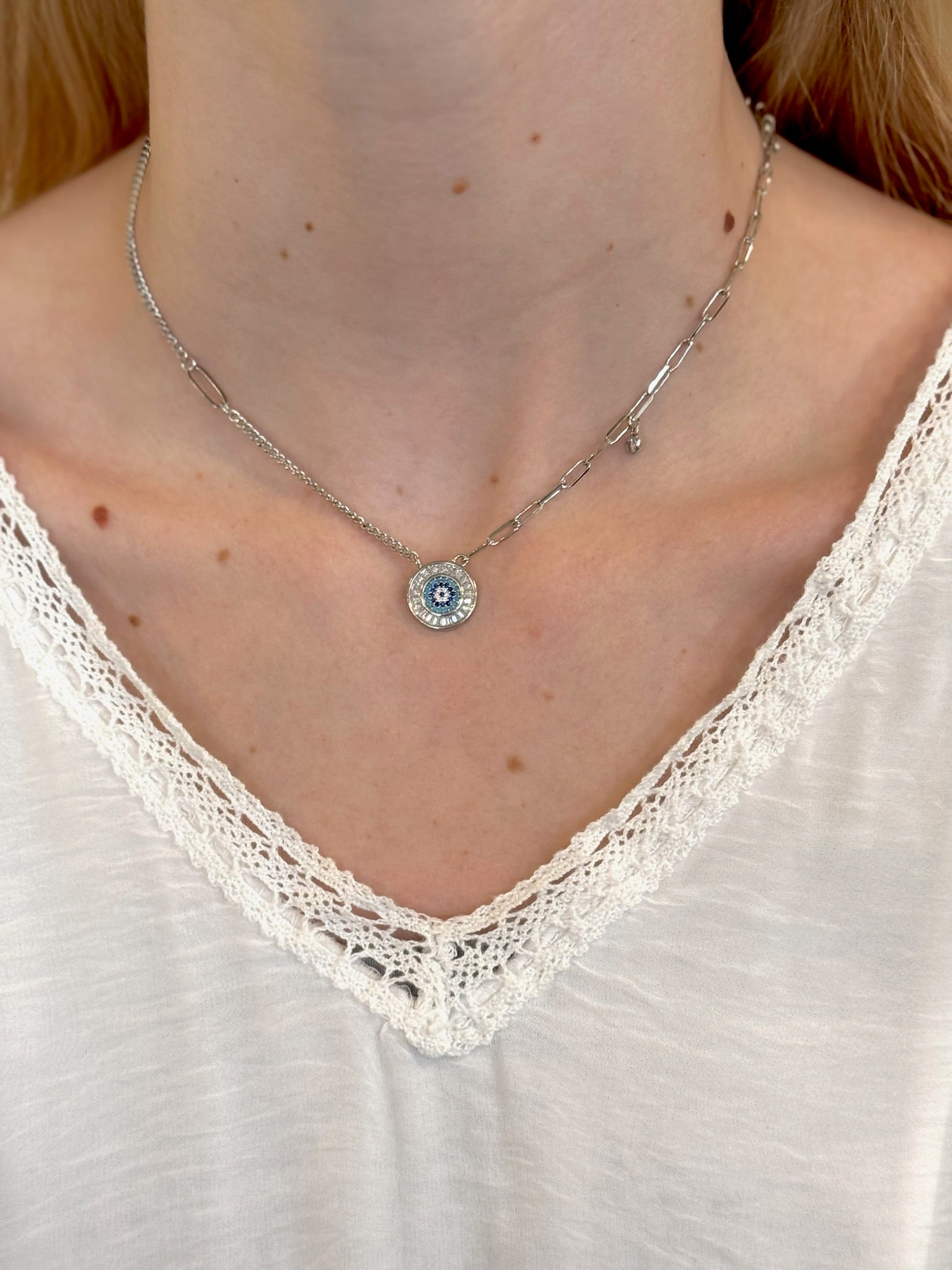 Necklace with a small pendant worn by a person in a white lace top
