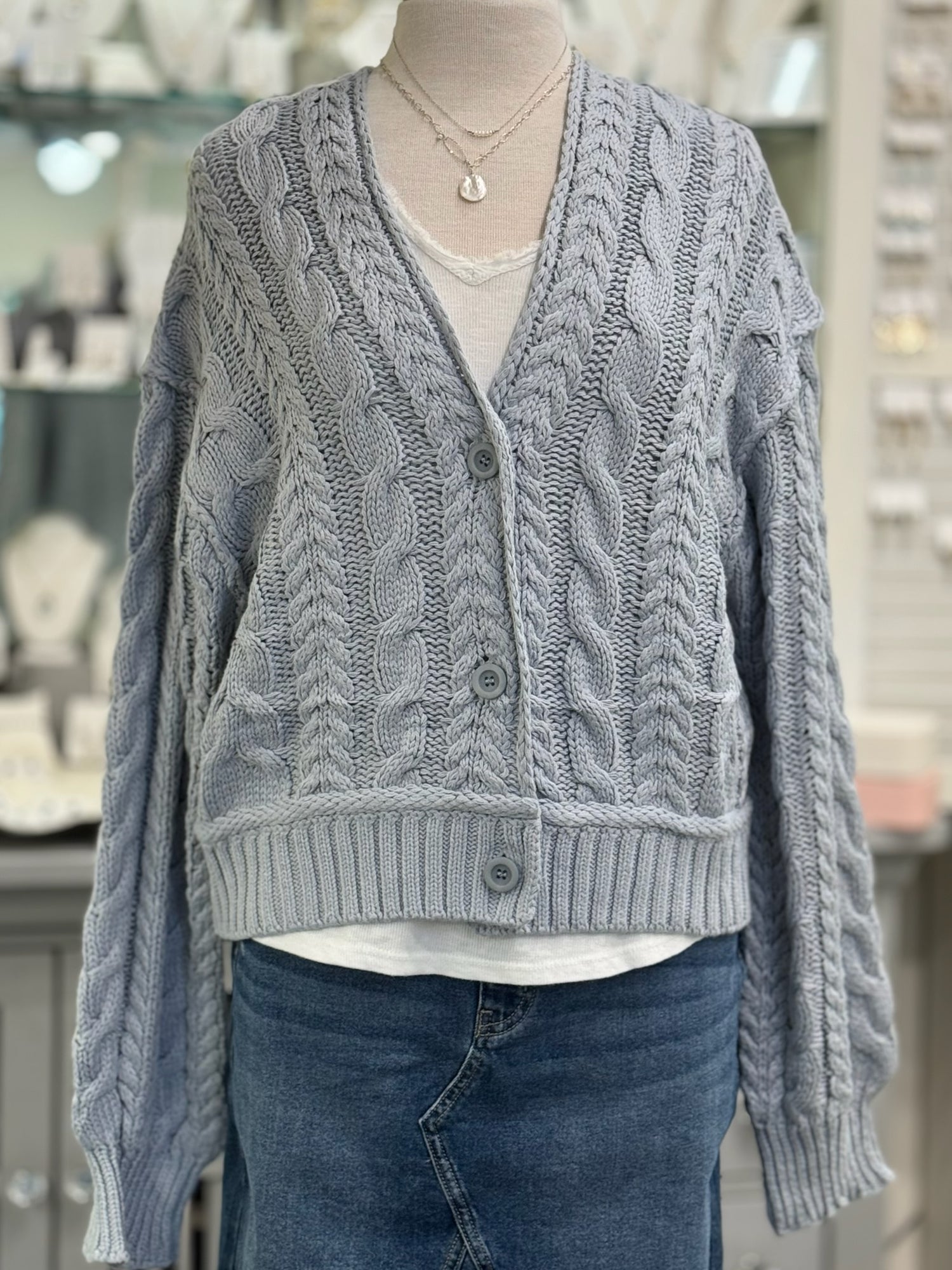 Mannequin wearing a gray cable knit cardigan with a blurred store interior background