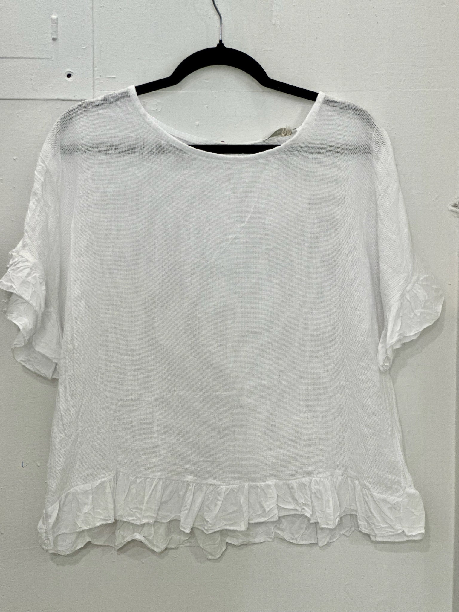 White blouse with ruffled sleeves and hem on a hanger against a white background