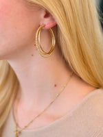 Close-up of a person wearing gold hoop earrings and a necklace.