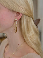 Woman wearing gold dangly earrings with linked, open shapes