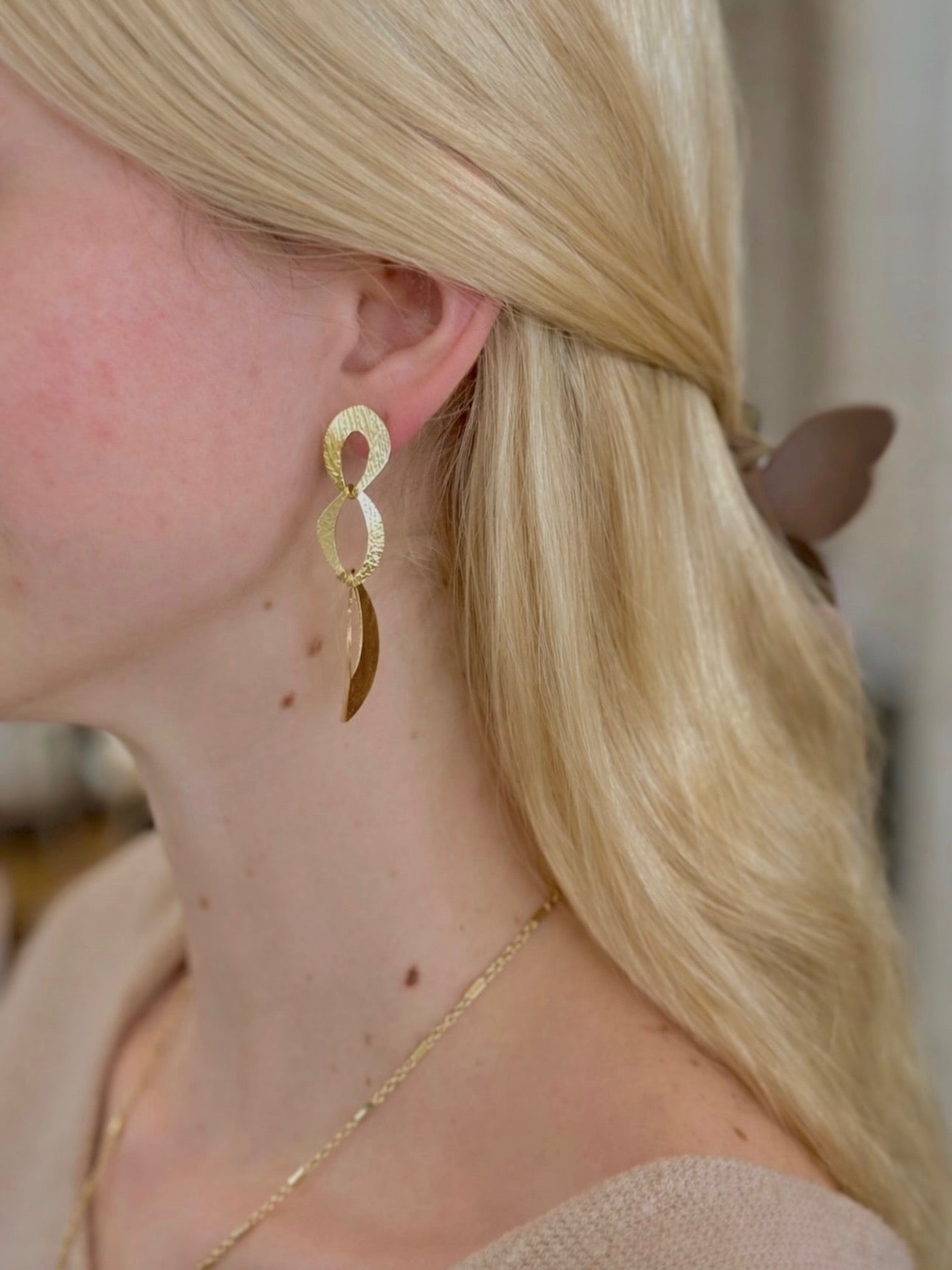 Woman wearing gold dangly earrings with linked, open shapes