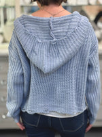 Light blue knitted sweater with a hood worn by a person, blurred background