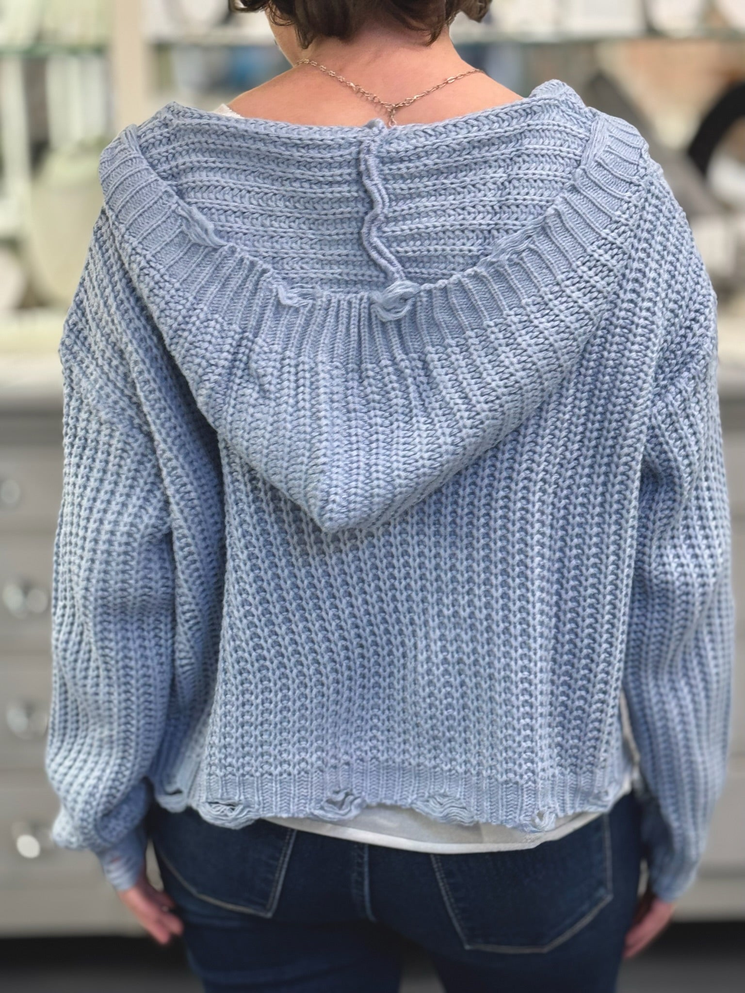 Light blue knitted sweater with a hood worn by a person, blurred background