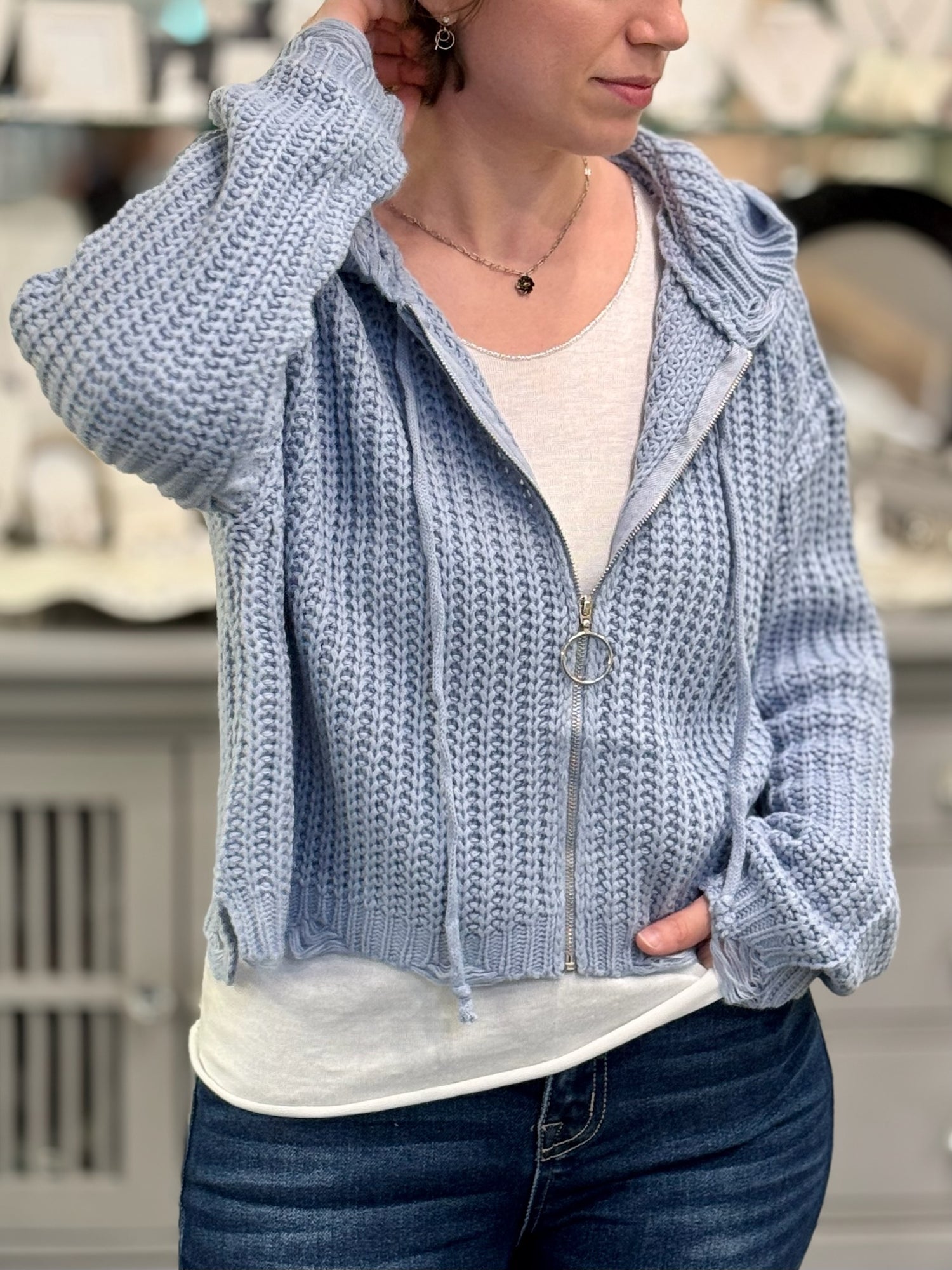 Person wearing a blue knitted hoodie with a blurred indoor background